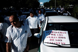 Taxi drivers walk past a sign that reads "We fight for the rights of taxi drivers" to protest the regulation of taxi apps like Uber in Cancun, Mexico on January 11, 2023. Reuters/Paola Ciomante