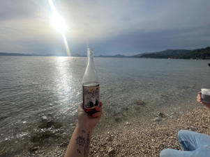 Croatian Zaton Bay at sunset with a bottle of Vina City, delicious and refreshing wine from the Dalmatian coast.